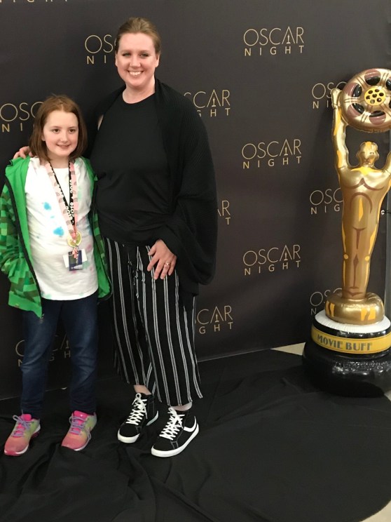 A girl, a mom, and an Oscar in front of an Oscar Night banner. 