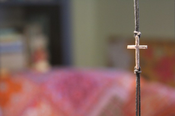 A cross on a necklace in foreground, chair and bookshelves in background