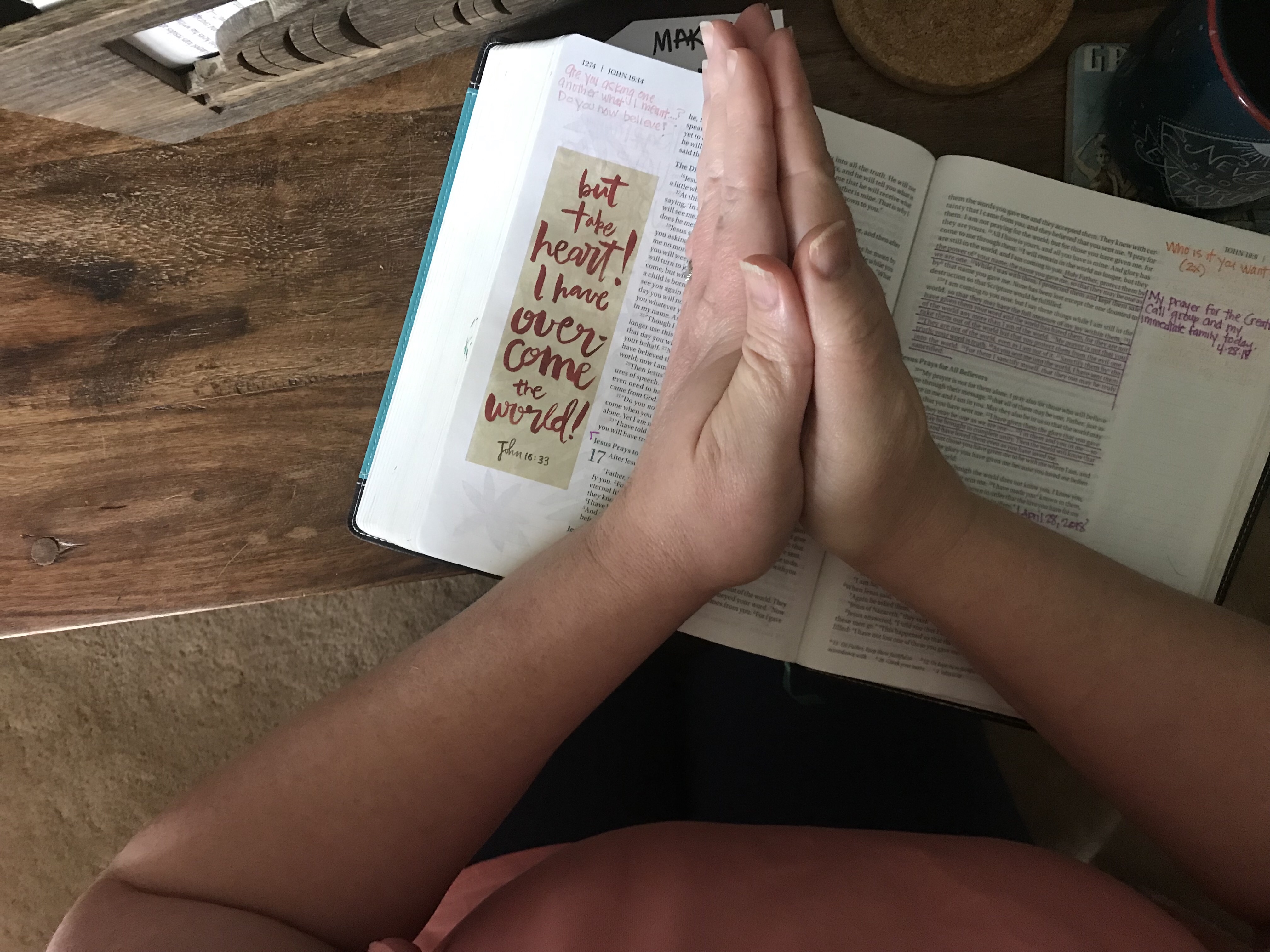 A bible with someone kneeling and hands laid across it as they pray