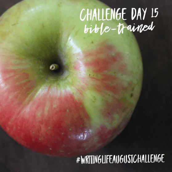 Top-down view of an apple on a wooden table. Photo text: Challenge Day 15, Bible-trained. #writinglifeaugustchallenge