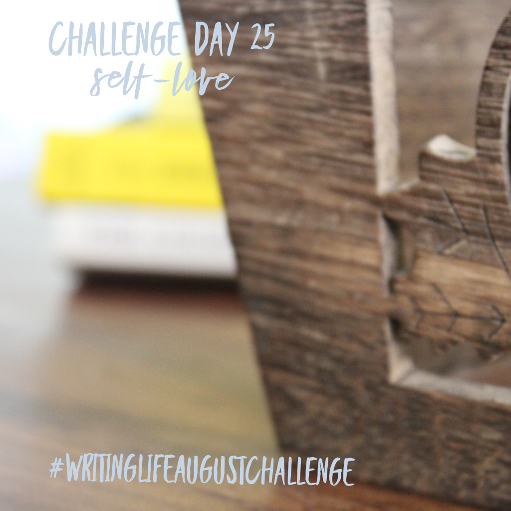Small decorative wooden crate on a table in foreground, with blurry, colorful books laying behind the crate in the background. Photo text: Challenge Day 25, self-love. #writinglifeaugustchallenge