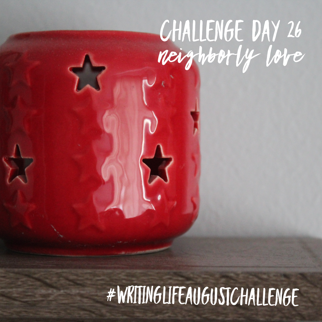 A red ceramic candle holder with star cut-outs sitting on a wooden wall shelf. Photo text: Challenge Day 26, neighborly love. #writinglifeaugustchallenge