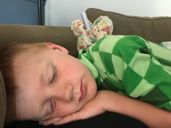 Sad boy lying on a couch with a heart-shaped pillow behind him. 